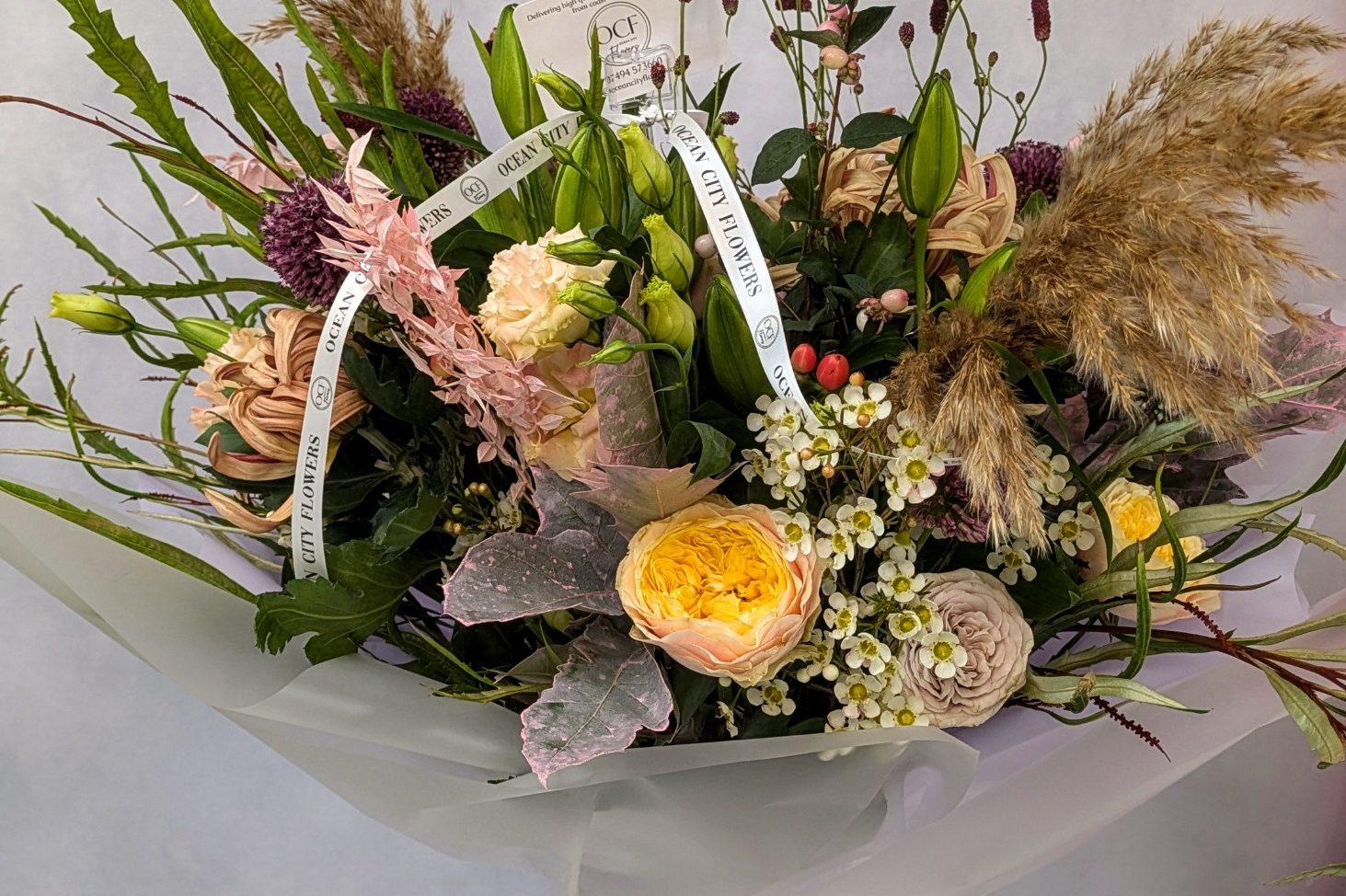 a bright and vibrant colourful floral bouquet containing electric blue delphiniums, scented coral peonies, yellow forsythia and complimenting rich coloured flowers and foliage. 